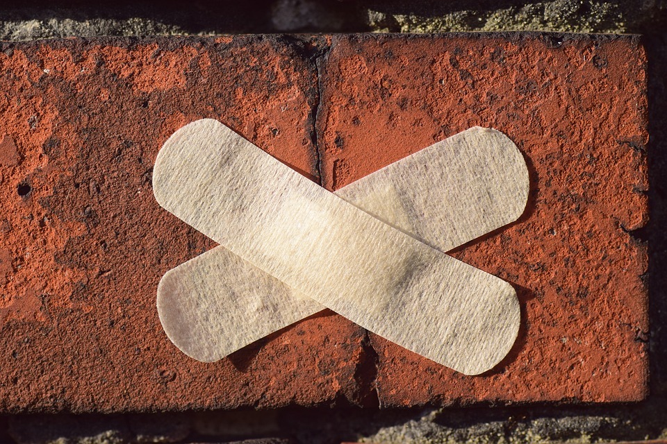 Mauer mit Pflaster drauf. Man sieht in nah aufnahme zwei pflaster die überkreuzt auf zwei ziegelsteinen kleben