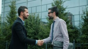 Zwei Personen begrüßen sich per Handschlag beim Bewerbungsgespräch vor einem Bürogebäude.