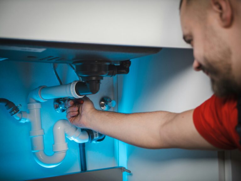 Handwerker repariert einen Siphon unter einem Waschbecken zum Thema Tätigkeitsschäden im Handwerk.